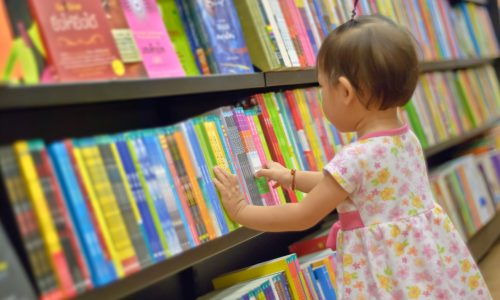 Asian Little girl is choosing a book in the library. A child is looking at the books in the library deciding which one to take home. Children creativity and imagination.